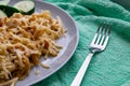 Long and wide pasta spaghetti noodles under viscous melted cheese on a platter with sliced Ã¢â¬â¹Ã¢â¬â¹fresh cucumbers on a bright green